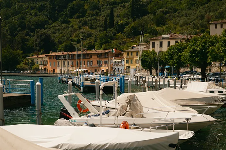 Motorbåtar i småbåtshamn framför en by vid en italiensk insjö